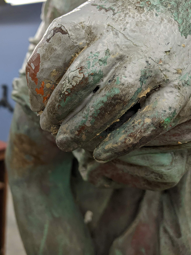 Close view of a hand on a sculpture. The index finger is slightly orange and larger than the adjacent fingers.